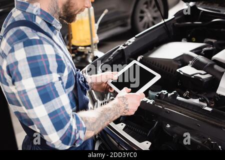 vue rognée du technicien tenant la tablette numérique près du moteur de la voiture compartiment Banque D'Images