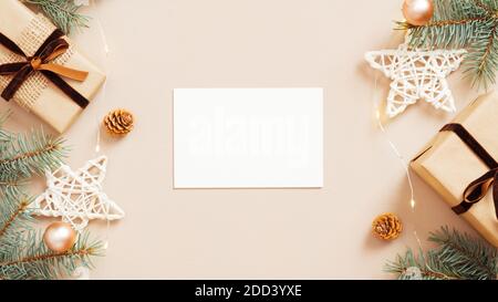 Composition de Noël à plat avec maquette de carte en papier vide, boîtes-cadeaux, décoration d'étoiles, branches de sapin sur fond beige. Table confortable, hyg Banque D'Images
