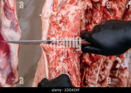 Boucher gros plan couper à la main la viande de mouton pendante dans la boutique de boucher. Des chattes coupés et pendus sur crochet dans un abattoir. Coupe halal. Banque D'Images