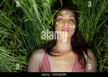 belle femme se trouve dans le champ de grain avec des fleurs sauvages et marguerite sur son visage Banque D'Images