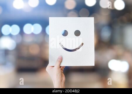 Main tenant le papier blanc avec émoticônes smiley (papier perforé) sur fond bokeh clair. Banque D'Images