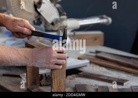 la main de l'homme fait marteler l'ongle sur le bureau en bois dans l'atelier avec arrière-plan de construction Banque D'Images