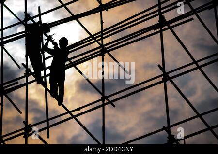 Silhouette de deux ouvriers du bâtiment portant des casques de sécurité sur un échafaudage contre le soleil par jour nuageux Banque D'Images