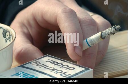 Gros plan d'une femme tenant une cigarette allumée à la main à côté d'un paquet de cigarettes de mélange Banque D'Images