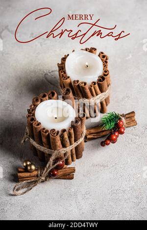 Bougies parfumées décorées de bâtons de cannelle près du lettrage joyeux noël sur fond gris texturé Banque D'Images