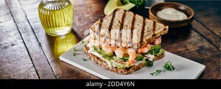 Sandwich de fruits de mer avec crevettes ou crevettes sur un lit de guacamole et salades vertes servies sur une table rustique une planche à découper dans une bannière panoramique ou hea Banque D'Images