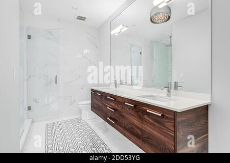 Une grande salle de bains luxueuse avec meuble-lavabo en bois, sol carrelé à motifs et portes de douche en verre. Banque D'Images