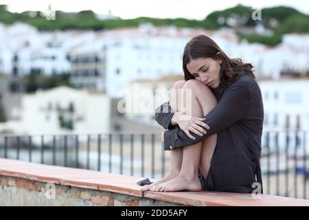 Portrait complet d'un adolescent triste se plaignant assis dessus une corniche dans une ville de plage