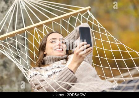 Bonne femme qui vérifie un téléphone portable allongé sur un hamac vacances en automne