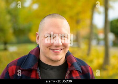 Souriant sympathique jeune homme dans un parc d'automne dans un gros plan de la tête et des épaules sur un feuillage jaune coloré sur les arbres Banque D'Images