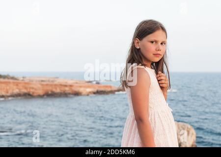 Petite fille en robe blanche debout sur la côte de la mer, portrait extérieur avec une mise au point sélective douce Banque D'Images