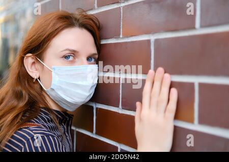 Portrait d'une femme en robe noire et un masque médical sur fond de mur de briques rouges Banque D'Images