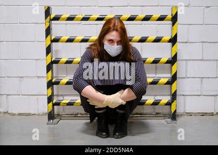 Une femme dans un masque médical est debout dans une impasse près d'une barrière de sécurité à rayures jaunes et noires, concept. Banque D'Images