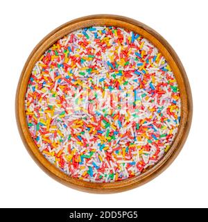 Arc-en-ciel saupoudrer dans un bol en bois. Saupoudrer de sucre coloré en forme de tige. Bonbons minuscules dans une variété de couleurs, utilisés comme décoration ou garniture. Gros plan. Banque D'Images