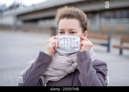 Portrait jeune femme européenne mise sur masque médical jetable de protection avec le texte manuscrit du coronavirus dans la rue de ville. Concept de coronavirus influ Banque D'Images