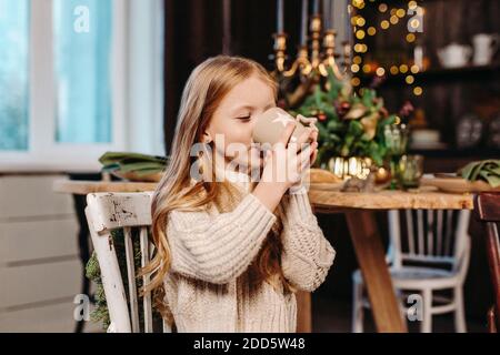 Petite fille qui boit du cacao avec des biscuits à la maison contre Noël arrière-plan Banque D'Images