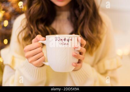 Une fille dans un chandail blanc et des leggings tient une grande tasse blanche dans ses mains Banque D'Images