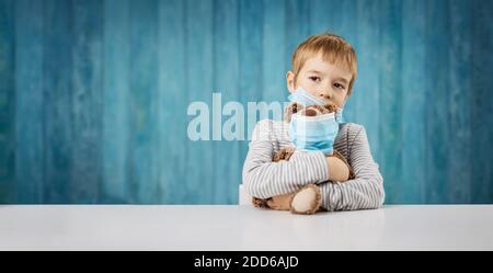 petit garçon assis avec un ours en peluche dans un visage médical masques Banque D'Images