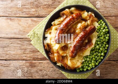 Saucisses frites avec purée de pommes de terre, sauce à l'oignon et petits pois dans une assiette sur la table. Vue horizontale du dessus Banque D'Images