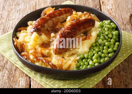 Cuisine britannique traditionnelle saucisses frites avec purée de pommes de terre, sauce à l'oignon et petits pois dans une assiette sur la table. Horizontale Banque D'Images