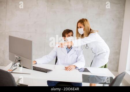 Médecins de couple avec des masques médicaux de protection du visage parlant et utilisation de l'ordinateur dans l'image Banque D'Images