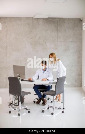 Médecins de couple avec des masques médicaux de protection du visage parlant et utilisation de l'ordinateur dans l'image Banque D'Images