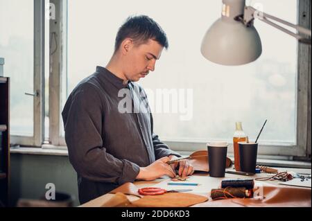 Un jeune cordonnier de la vieille école remplit un ordre de fabriquer un produit en cuir exclusif. Portrait en studio. Banque D'Images