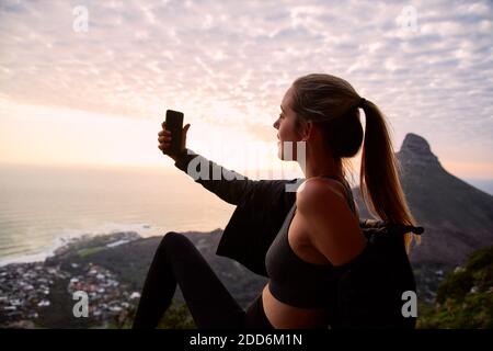 Jeune femme en vacances portant un sac à dos marchant le long du chemin côtier au coucher du soleil ou au lever du soleil, prendre le selfie pour publier sur le social multimédia avec téléphone portable Banque D'Images