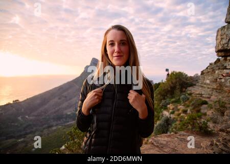 Portrait de la jeune femme en vacances marchant le long du chemin côtier comme le soleil se couche sur la mer derrière elle Banque D'Images