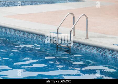 approche d'une piscine avec de l'eau propre bleue, avec quelques escaliers en métal à côté d'un plancher brun, dans la journée avec réflexion dans l'eau Banque D'Images