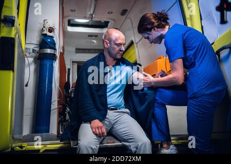 Une jeune infirmière en uniforme qui donne une injection à un patient dans une voiture d'ambulance. Banque D'Images