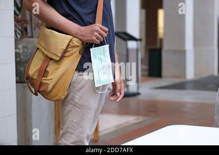 Gros plan d'un jeune homme dans une ville tenue de rue un masque chirurgical dans sa main Banque D'Images