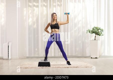 Portrait d'une jeune femme blonde qui fait un pas d'exercice aérobie avec une haltère à la maison Banque D'Images