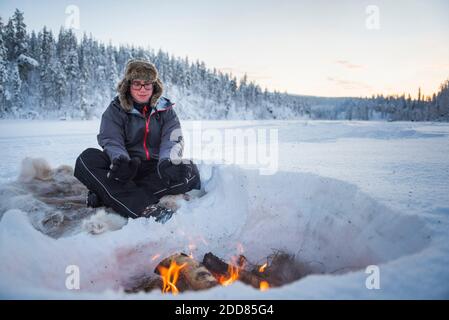 Personne assise à un feu de camp se réchauffant lui-même par un froid glacial en hiver dans le cercle arctique de Laponie, en Finlande Banque D'Images