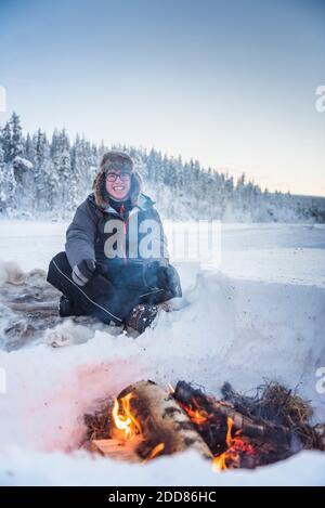 Personne assise à un feu de camp se réchauffant lui-même par un froid glacial en hiver dans le cercle arctique de Laponie, en Finlande Banque D'Images