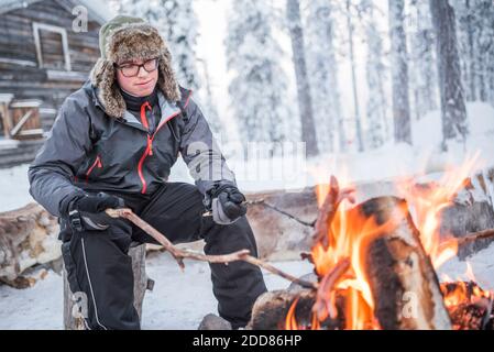 Personne assise à un feu de camp se réchauffant lui-même par un froid glacial en hiver dans le cercle arctique de Laponie, en Finlande Banque D'Images