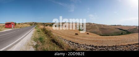 Panorama du paysage de Toscane en été avec la route, maison rouge abandonnée (maison de l'inspecteur de route) à gauche et balles de foin à droite. Plus de 10.00 ans Banque D'Images