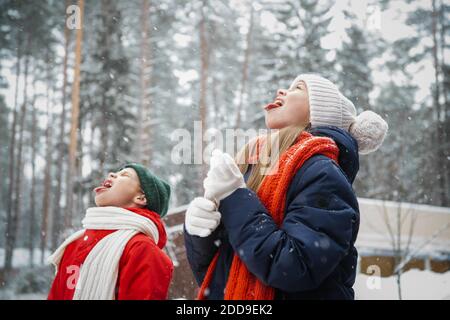 Un écolier et une fille d'école apprécient leurs vacances de Noël, marcher pendant la chute de neige et attraper les flocons de neige qui tombent dans leur bouche Banque D'Images