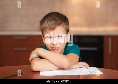 7 yeas vieux garçon assis à une table dans la cuisine et pleurer tout en travaillant sur des devoirs difficiles Banque D'Images