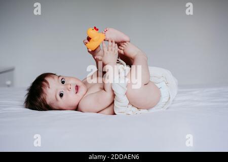 Bébé garçon mignon jouant avec un jouet de canard tout en étant allongé sur le lit à la maison Banque D'Images