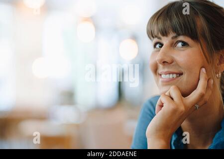 Femme entrepreneur souriante regardant loin avec la main sur le menton assis dans le café Banque D'Images