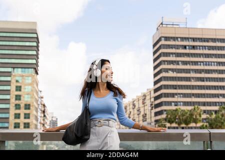 Belle jeune femme d'affaires qui écoute de la musique à l'aide d'un casque tout en s'appuyant sur main courante Banque D'Images