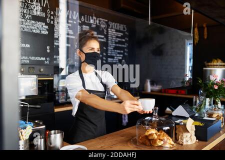 Serveuse portant un masque de protection tout en donnant du café au café Banque D'Images