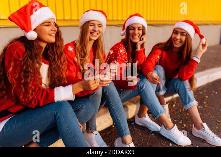 Compagnie de jeunes femmes gaies célébrant le nouvel an en chapeaux de Père Noël, avec des spamisseurs
