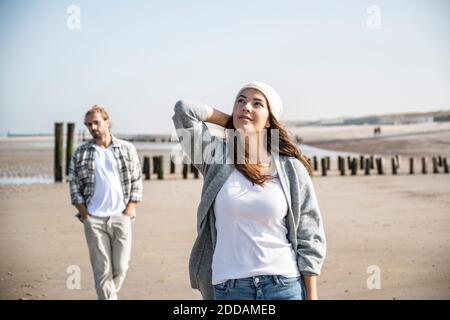 Jeune femme attentionnés regardant pendant que l'homme marche en arrière-plan à la plage Banque D'Images