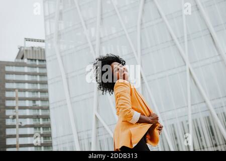 Femme entrepreneur souriante avec les yeux fermés debout contre le bâtiment de bureau Banque D'Images