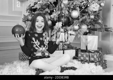 Enfant célébrer Noël à la maison. Traditions d'hiver. Boutique cadeaux concept. Porter le chandail de Noël pour enfants adorables. Bénéficiant d''hiver. Décor d'attributs de Noël. Petite fille près de l'arbre de Noël. Banque D'Images