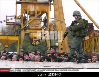 PAS DE FILM, PAS DE VIDÉO, PAS DE TV, PAS DE DOCUMENTAIRE - © FLASH 90/KRT/ABACA. 54815-3. Gaza-Israël, 14 janvier 2004. Un agent de police des frontières israélien se tient devant les travailleurs palestiniens pendant qu'ils attendent de quitter la zone industrielle au passage d'Erez le 14 janvier 2004. Une mère palestinienne de deux personnes à blouts Banque D'Images