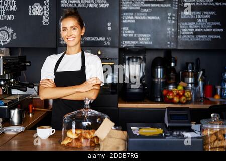 Portrait d'une serveuse souriante avec bras croisés travaillant au café Banque D'Images