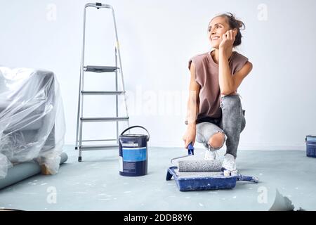 Jeune femme tête dans les mains tenant le rouleau de peinture dans la peinture plateau lors du accroupi à la maison Banque D'Images